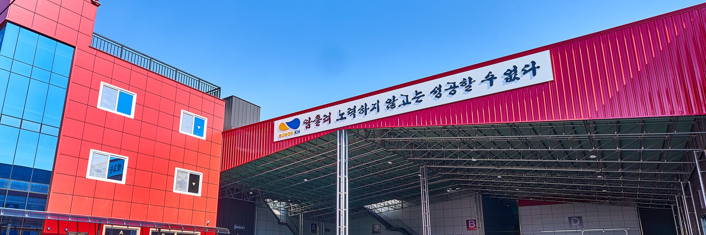 「땀흘려 노력하지 않고는 성공할 수 없다」 간판이 걸린 부원KH 신축공장 입구와 빨간 사무동